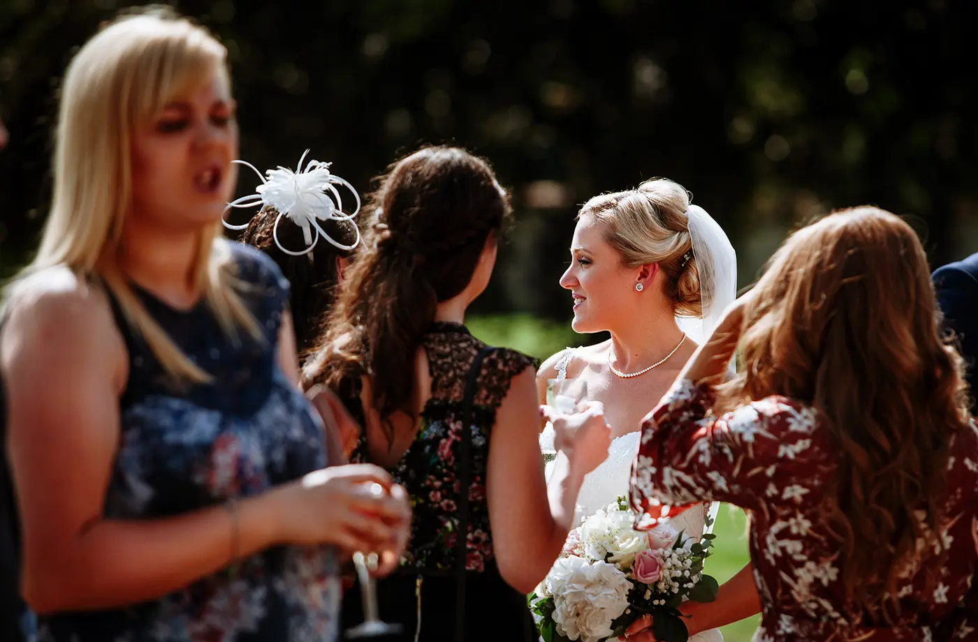 Bride Sally seen through a group of guests in beautiful natural light at Stubton Hall, Nottinghamshire, a creative documentary portrait by Gary Phillip