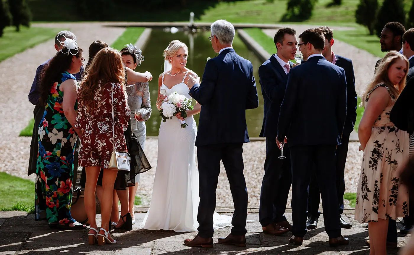 Bride Sally with her family group in front of the ornamental pond at Stubton Hall, Nottinghamshire, a formal family portrait by documentary photographer Gary Phillip