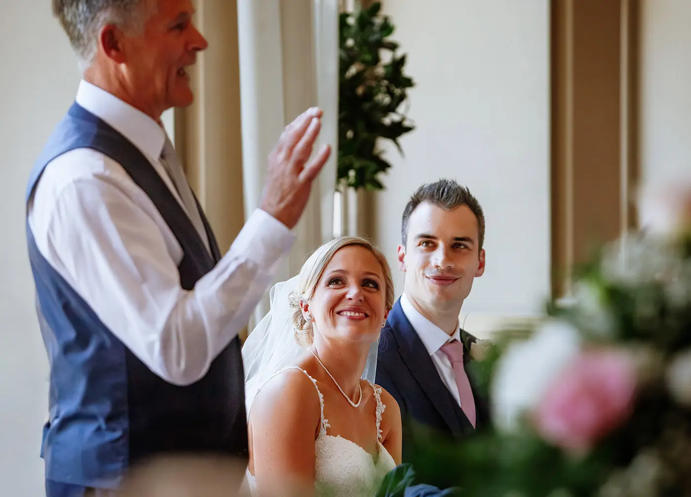 Bride Sally and groom Luke listening to the father of the bride speech with big smiles at Stubton Hall, Nottinghamshire, candid wedding breakfast photography by Gary Phillip
