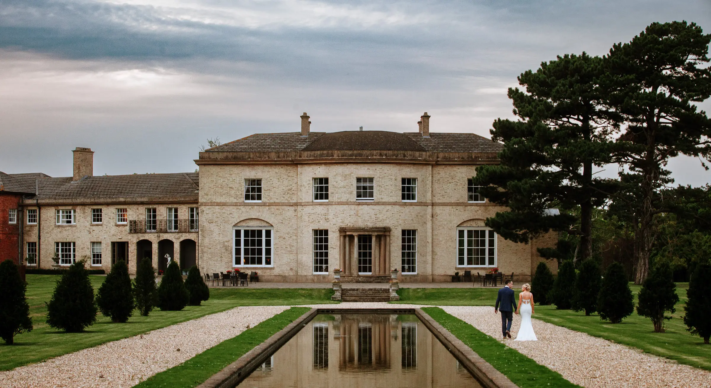 Bride Sally and groom Luke walking together around the ornamental pond at Stubton Hall, Nottinghamshire, relaxed couple portrait photography by Gary Phillip