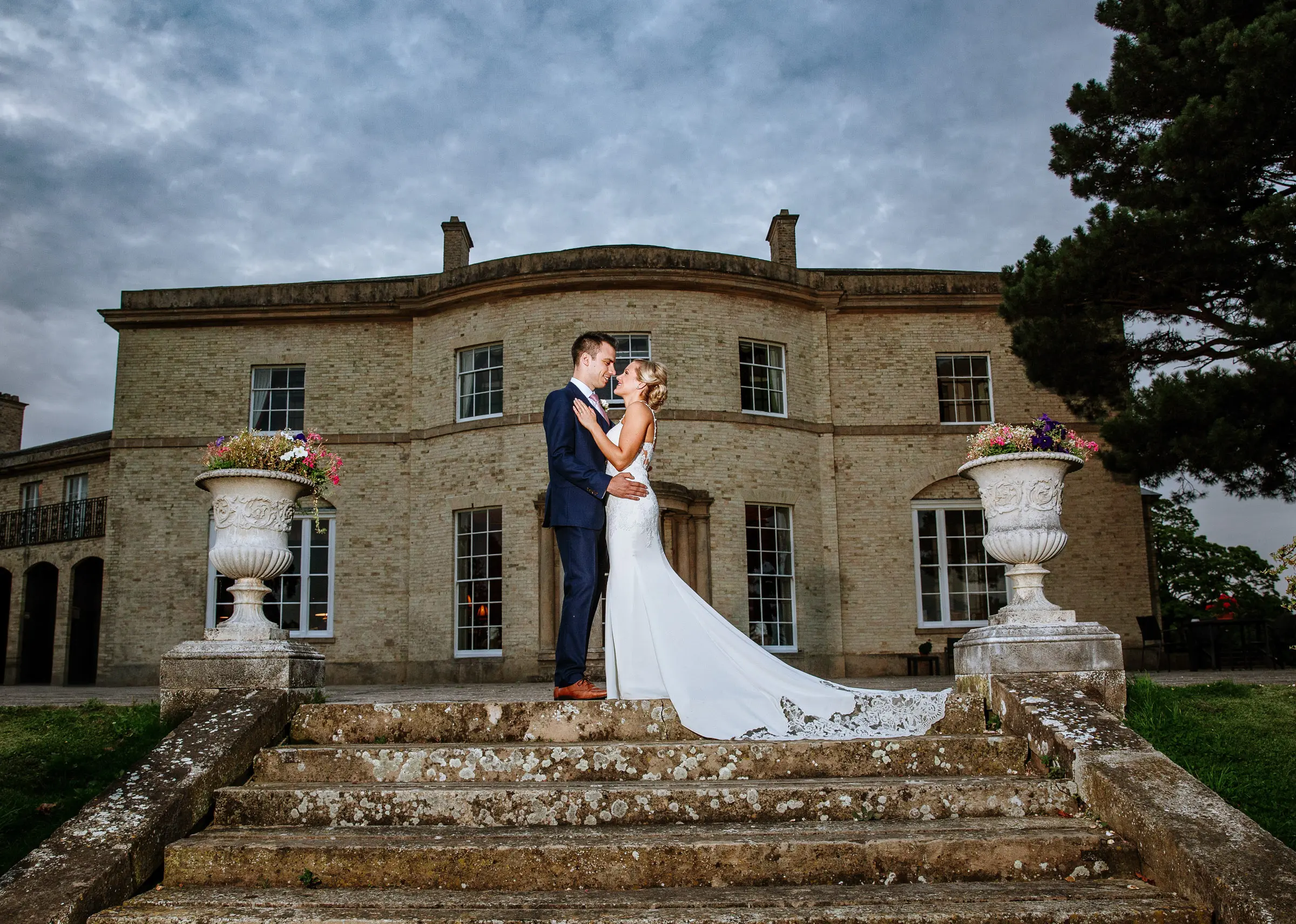 Portrait of bride Sally and groom Luke standing at the top of the steps with Stubton Hall in the background, documentary wedding photography by Gary Phillip, Nottinghamshire
