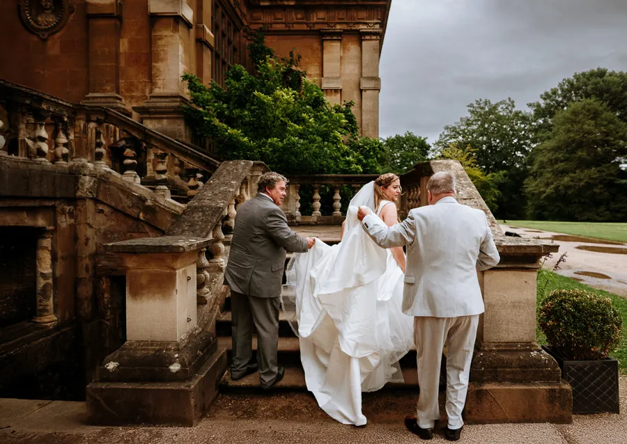 Bride arriving at Wollaton Hall, helped with her dress on the stone steps