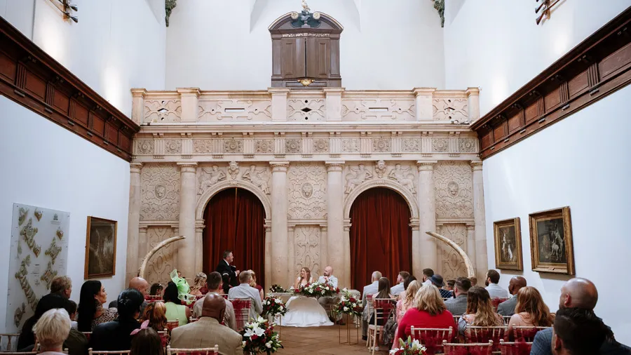 The ceremony room at Wollaton Hall — carved stone arcades, red curtains, a full room of guests