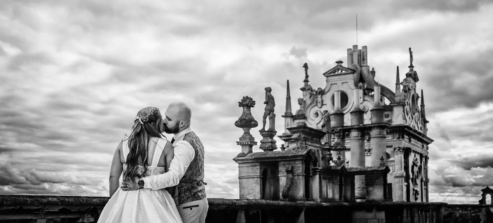 Amy and Andy kissing on the roof of Wollaton Hall, Elizabethan chimney stacks and a dramatic sky behind them